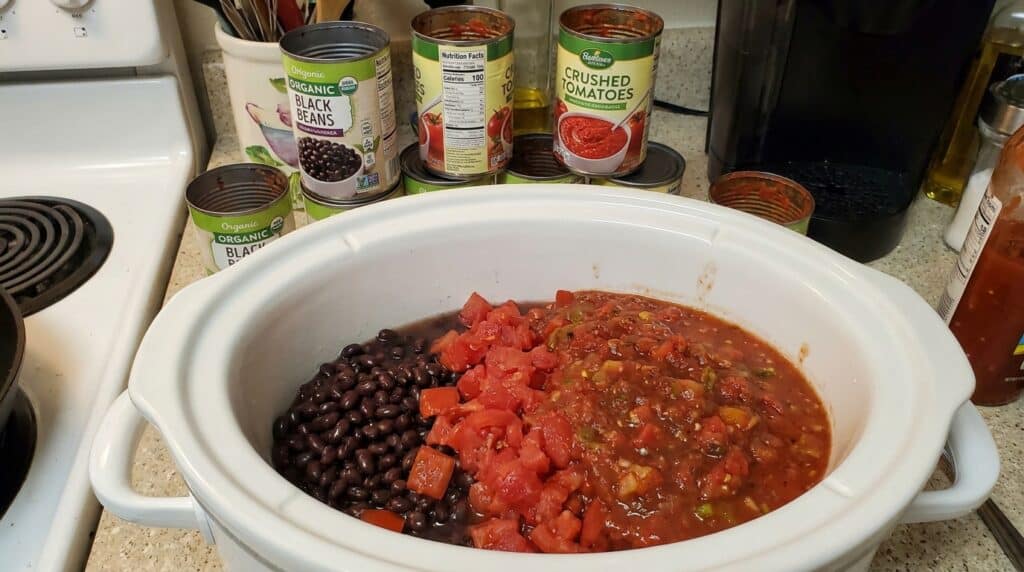Slow cooker insert filled with beans tomatoes and salsa before the lid goes on