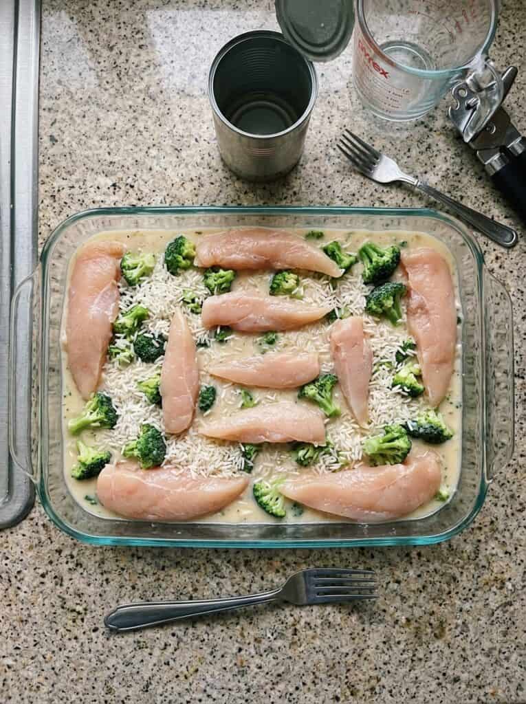 Whole chicken tenderloins on uncooked rice and frozen broccoli in a 9x13 glass dish before bakingtfr43crfzwe